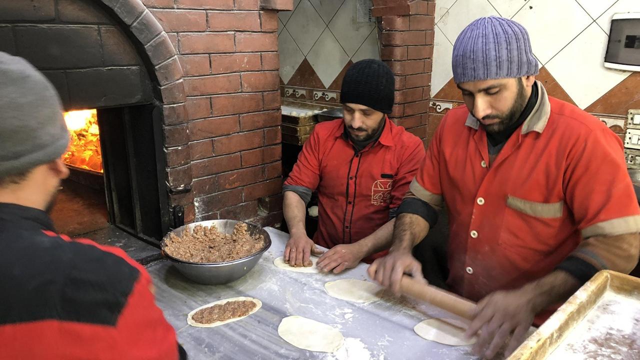 Drei Männer stehen in der syrischen Stadt Duma an einem Pizzaofen.