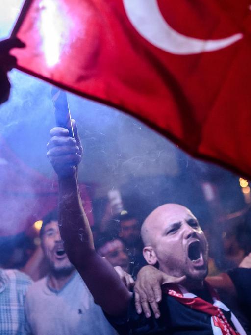 Männer in einer Menschenmenge in der Dunkelheit. Sie rufen und schwenken die türkische Flagge.