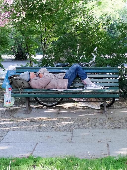 Auf einer Parkbank am Olivaer Platz schläft ein älterer Mann auf Zeitungen.