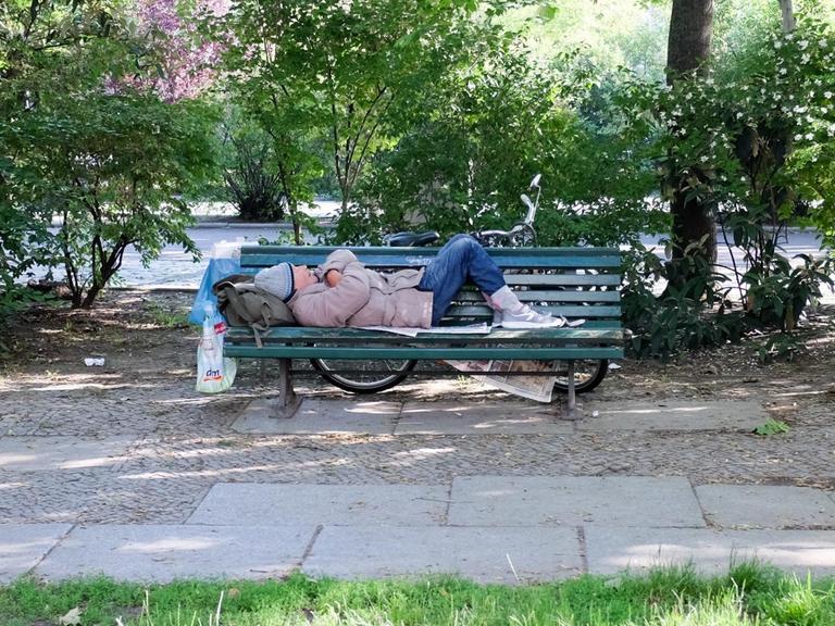 Auf einer Parkbank am Olivaer Platz schläft ein älterer Mann auf Zeitungen.