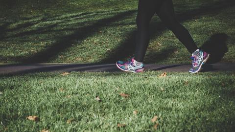 Zu sehen sind Beine mit Laufschuhen auf einer Wiese 