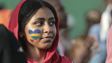 Aufnahme einer Frau mit einem geschminkten Herz auf der Wange in den Farben der alten sudanesischen Flagge.