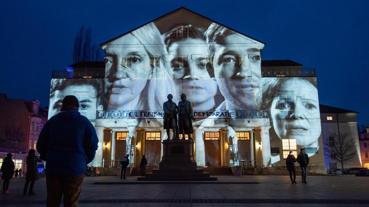 Besucher vor dem Deutschen Nationaltheater Weimar zur Eröffnung der Woche der Demokratie. Gesichter verschiedener Menschen werden auf das Gebäude projiziert.