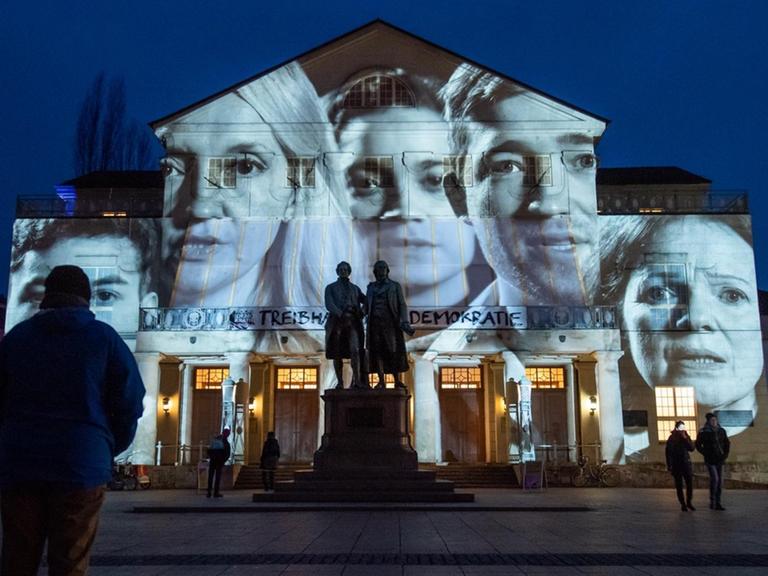Besucher vor dem Deutschen Nationaltheater Weimar zur Eröffnung der Woche der Demokratie. Gesichter verschiedener Menschen werden auf das Gebäude projiziert.