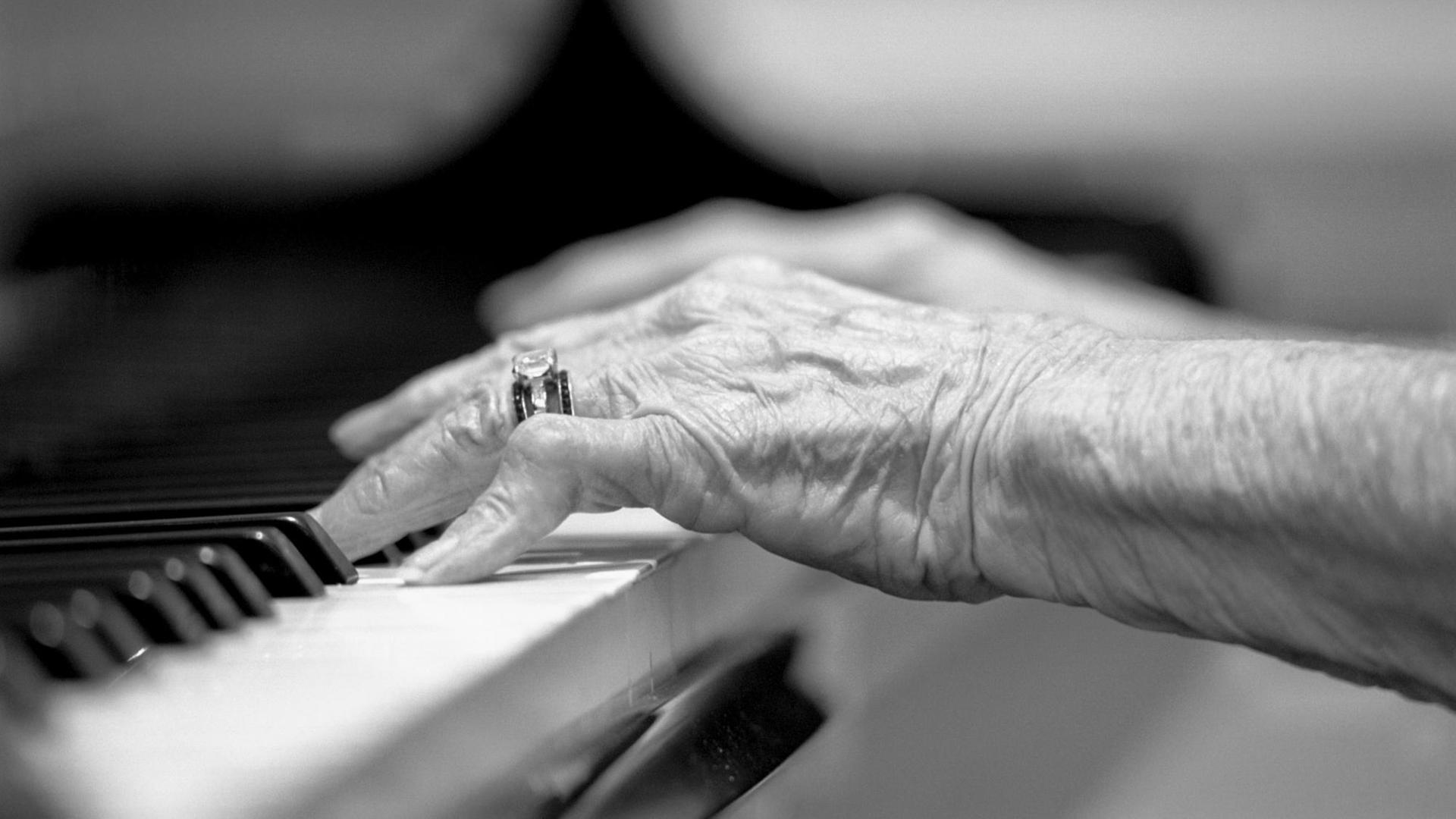 Hände einer älteren Frau auf einer Klaviertastatur.