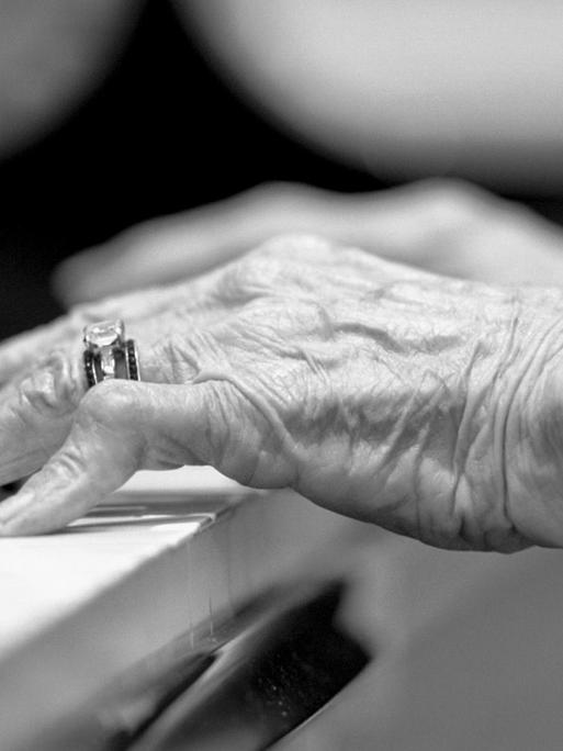Hände einer älteren Frau auf einer Klaviertastatur.