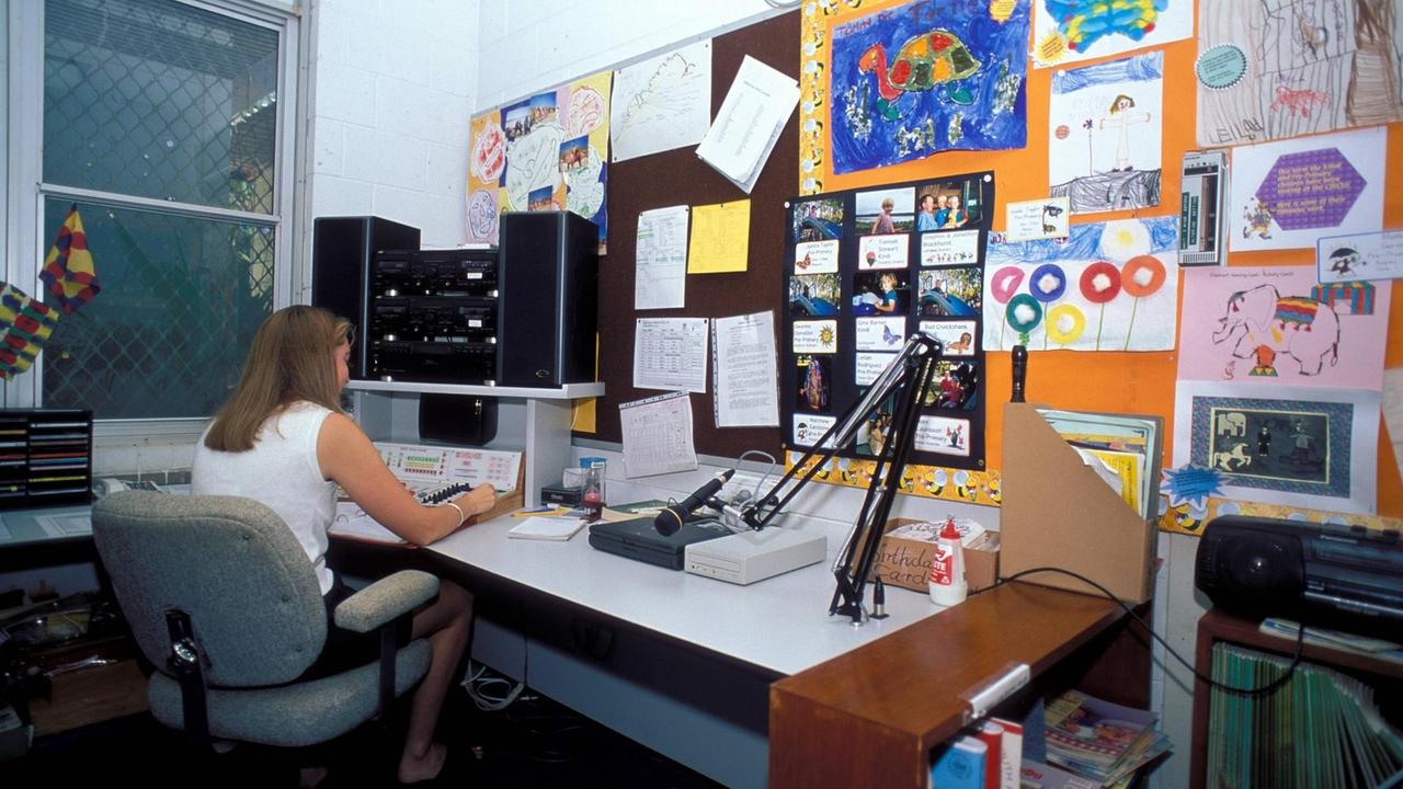 Ein Frau mit langen Haaren sitzt an einem Schreibtisch. An der Wand hängen Kinderzeichnungen. 