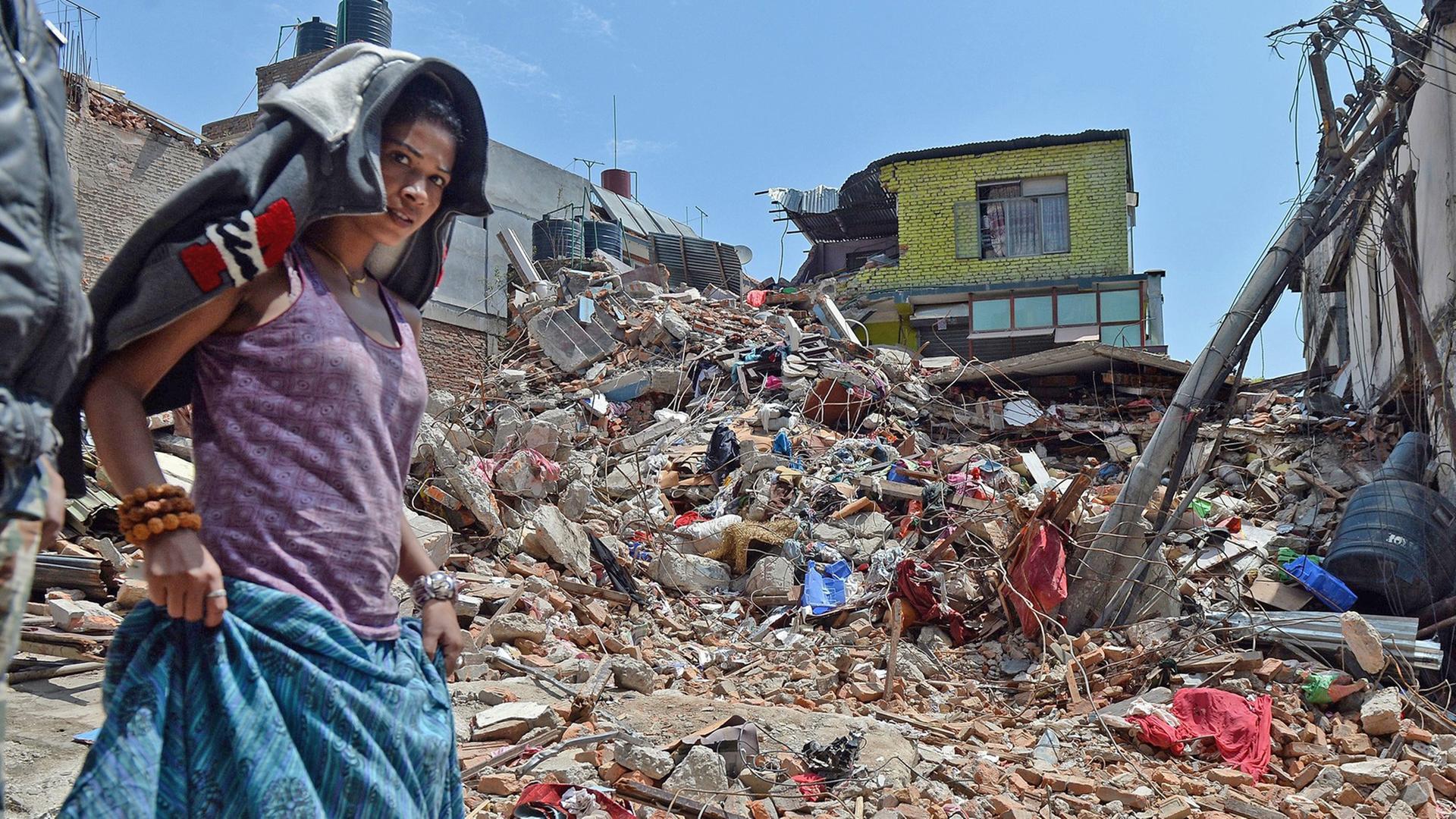 Eine Frau in Nepal läuft an einem zerstörten Haus vorbei. 