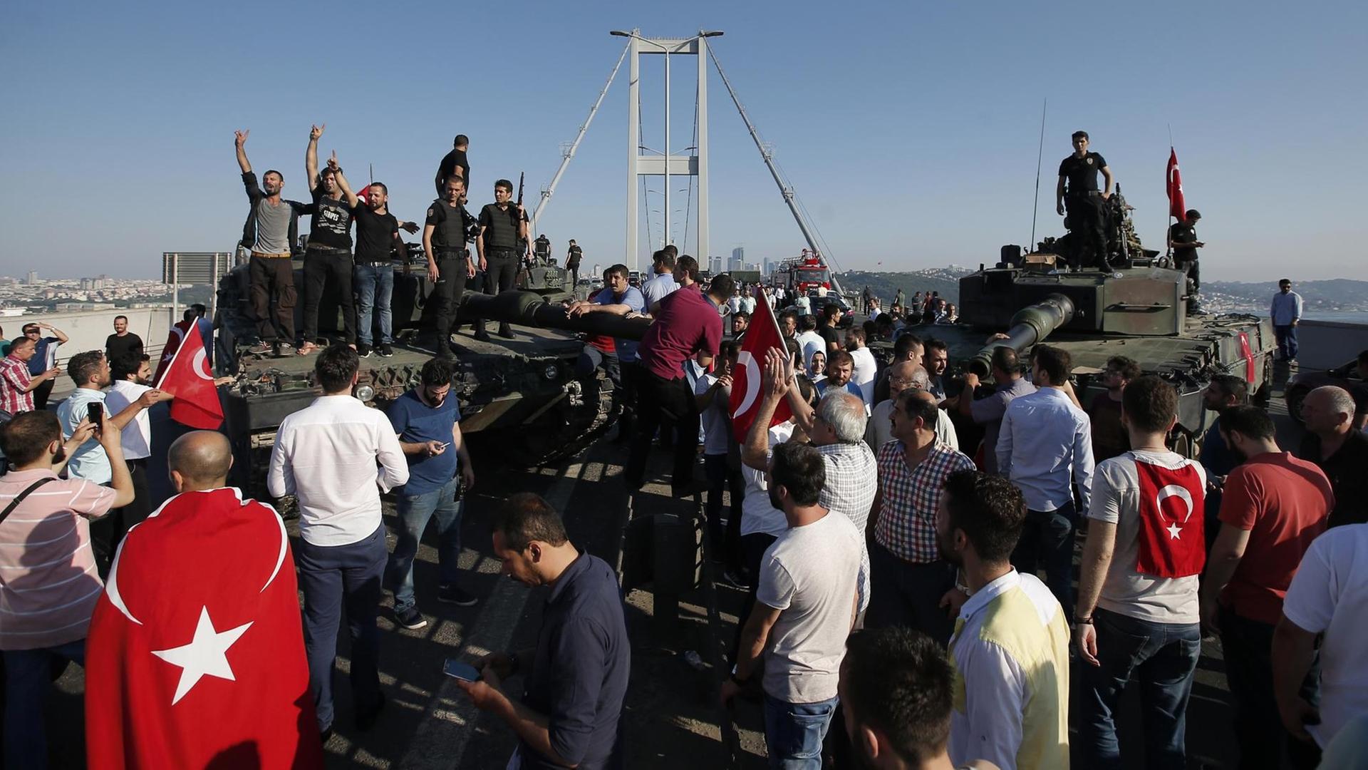 Menschen in Istanbul stehen um und auf Panzern des türkischen Militärs. Im Hintergrund die Bosporus-Brücke.