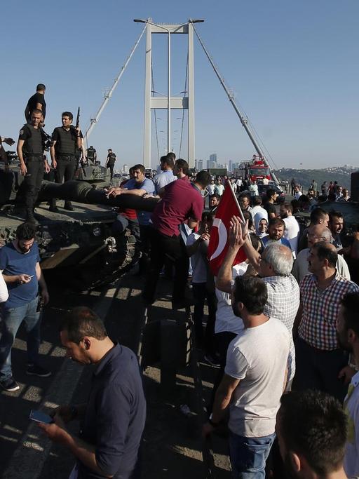 Menschen in Istanbul stehen um und auf Panzern des türkischen Militärs. Im Hintergrund die Bosporus-Brücke.
