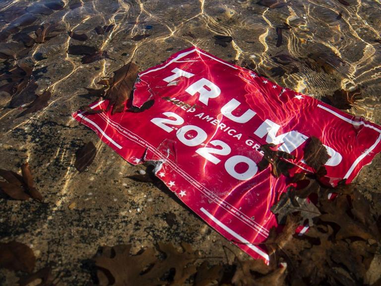 Ein rotes Wahlkampfplakat "Trump 2020" liegt zerfleddert im Wasser vor dem Kapitol Gebäude in Washington D.C., 9.1.2021.