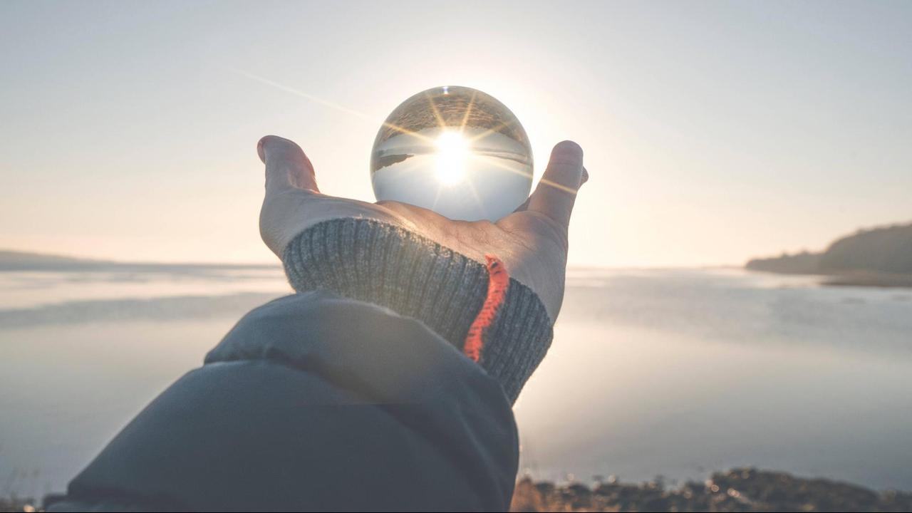 Das Foto zeigt eine Hand, die eine Glaskugel hält, in der das Sonnenlicht reflektiert wird.