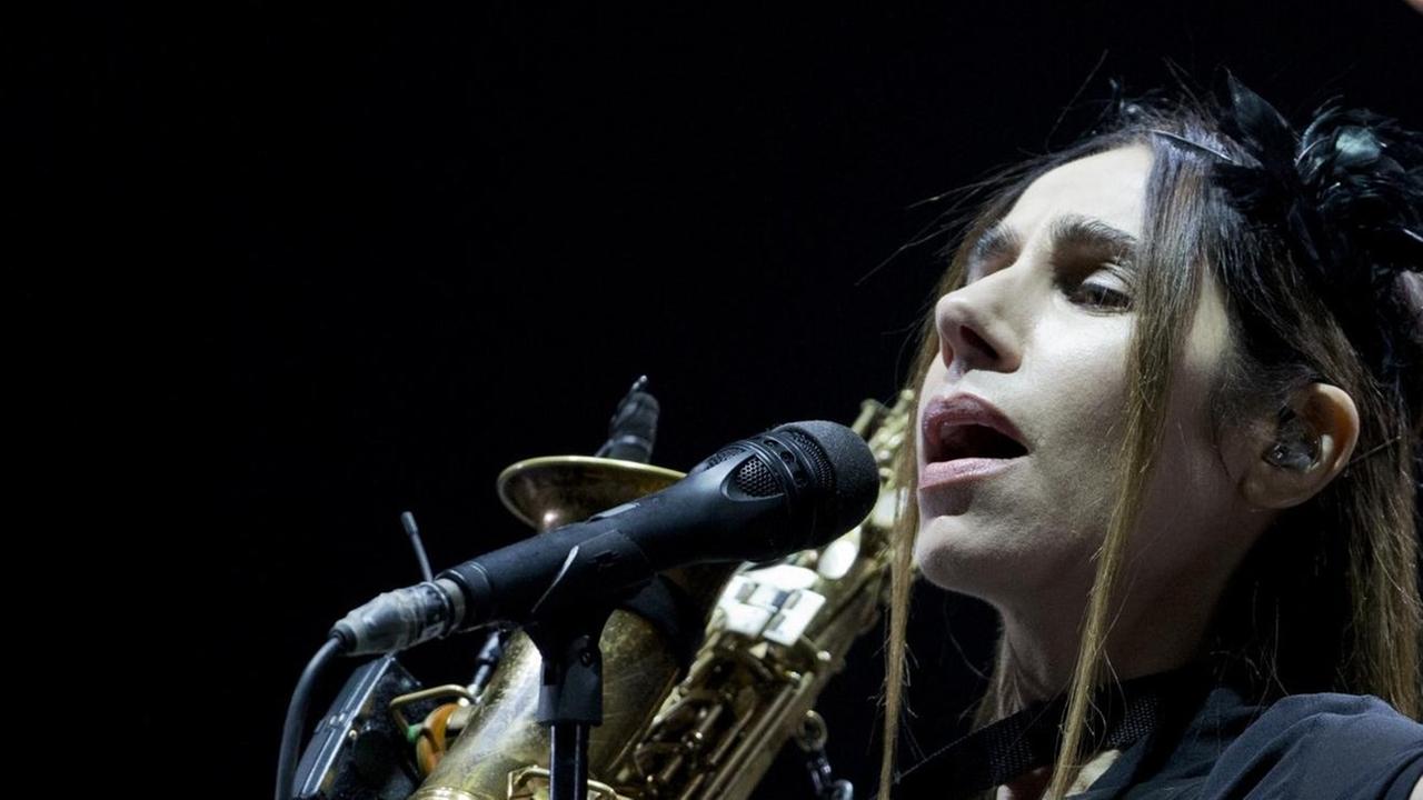 PJ Harvey steht vor einem Mikrophon mit einem Saxophon in der Hand.