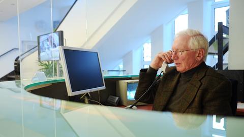 Ein Senior sitzt im Büro an einem Empfang und telefoniert.