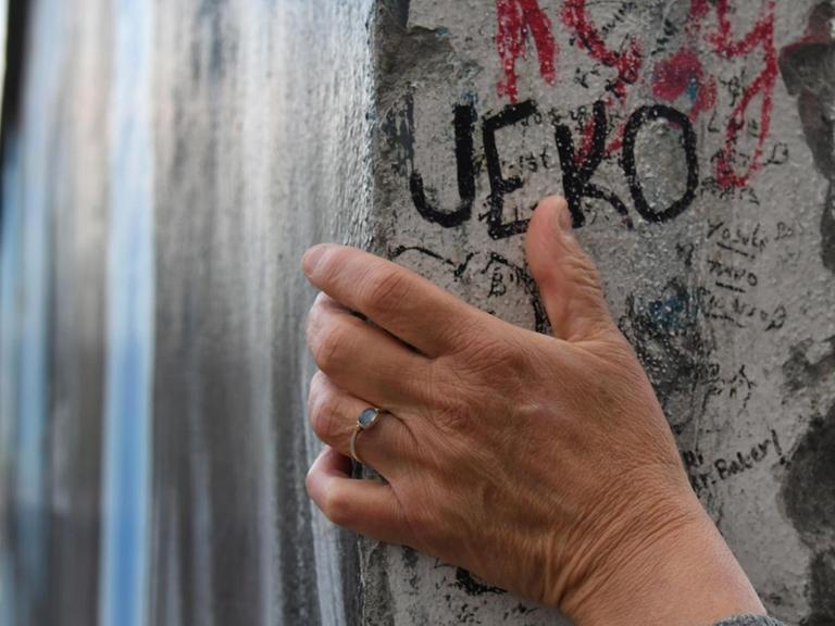 Eine Hand ruht auf einem Teil der Berliner Mauer.