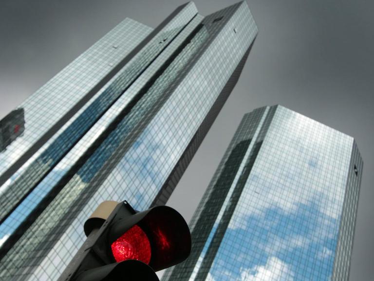 Eine rote Verkehrsampel vor der Zentrale des Unternehmens mit schwarzen Regenwolken im Bankenviertel in Frankfurt am Main.