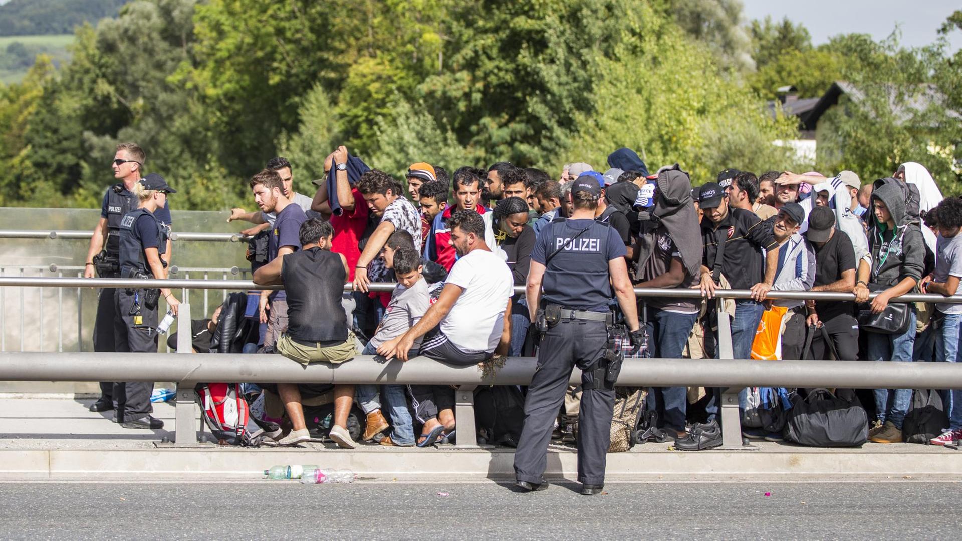 Zahlreiche Flüchtlinge warten am Grenzübergang zwischen Österreich und Deutschland in Freilassing (Bayern) darauf, nach Deutschland zu gelangen. Polizisten stehen vor und neben ihnen.