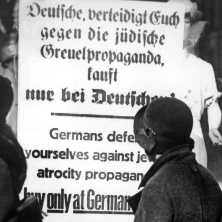 Drei deutsche Frauen lesen im April 1933 ein Plakat am Schaufenster eines Geschäfts, das zum Boykott von jüdischen Geschäften aufruft: "Deutsche, verteidigt Euch gegen die jüdische Greuelpropaganda, kauft nur bei Deutschen!"