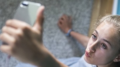 Ein blondes attraktives Mädchen sitzt in ihrem Zimmer auf dem Boden und macht Selfies 