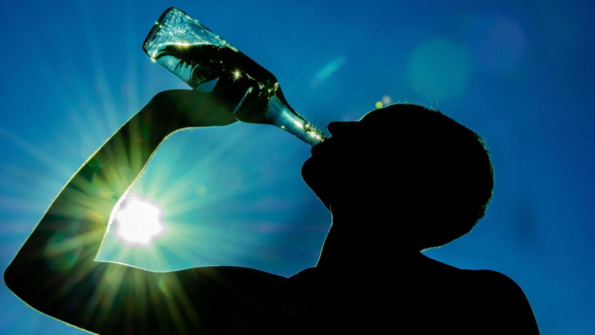 Ein Mann trinkt aus einer Wasser-Flasche. Durch seinen Arm scheint die Sonne.
