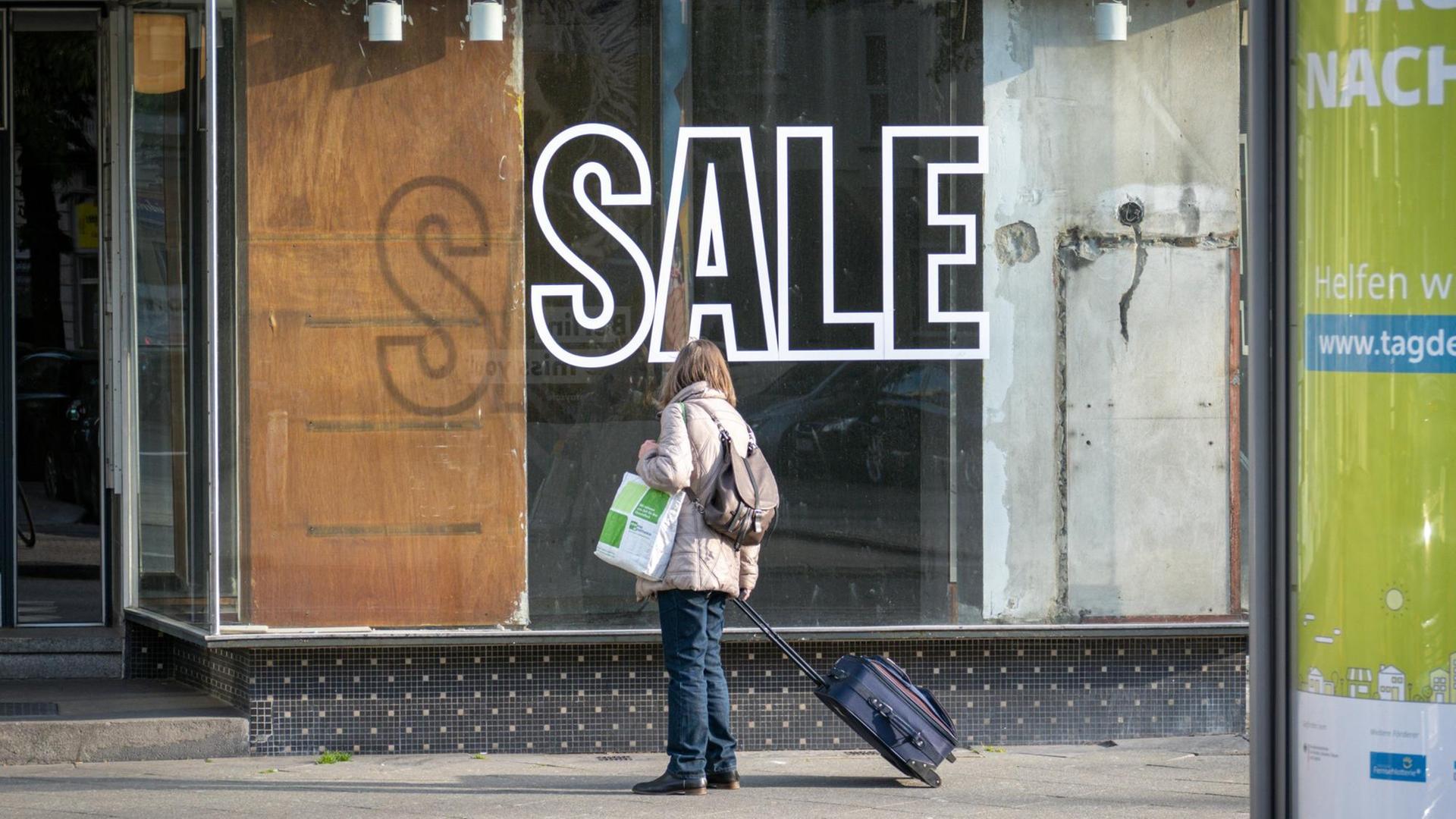 Zu sehen ist eine Frau vor einem Geschäft mit leerem Schaufenster und der Aufschrift "Sale".