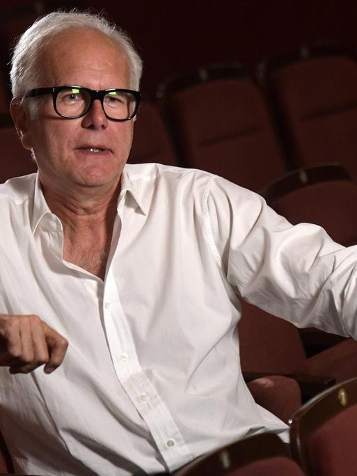 Harald Schmidt trägt ein weißes Hemd und sitzt auf die Bühne blickend alleine im Parkett eines Theaters.