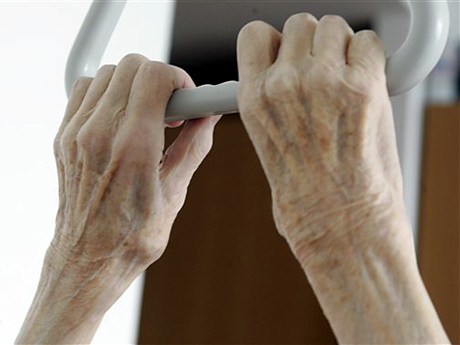 Die Hände einer pflegebedürftigen Frau umfassen in einem Seniorenheim in Stuttgart den Haltegriff über ihrem Bett.