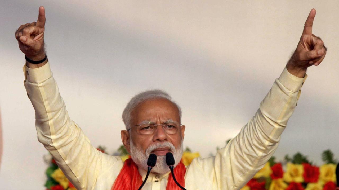 Narendra Modi steht am Mikrofon und hebt die Arme adressierend in die Luft.
