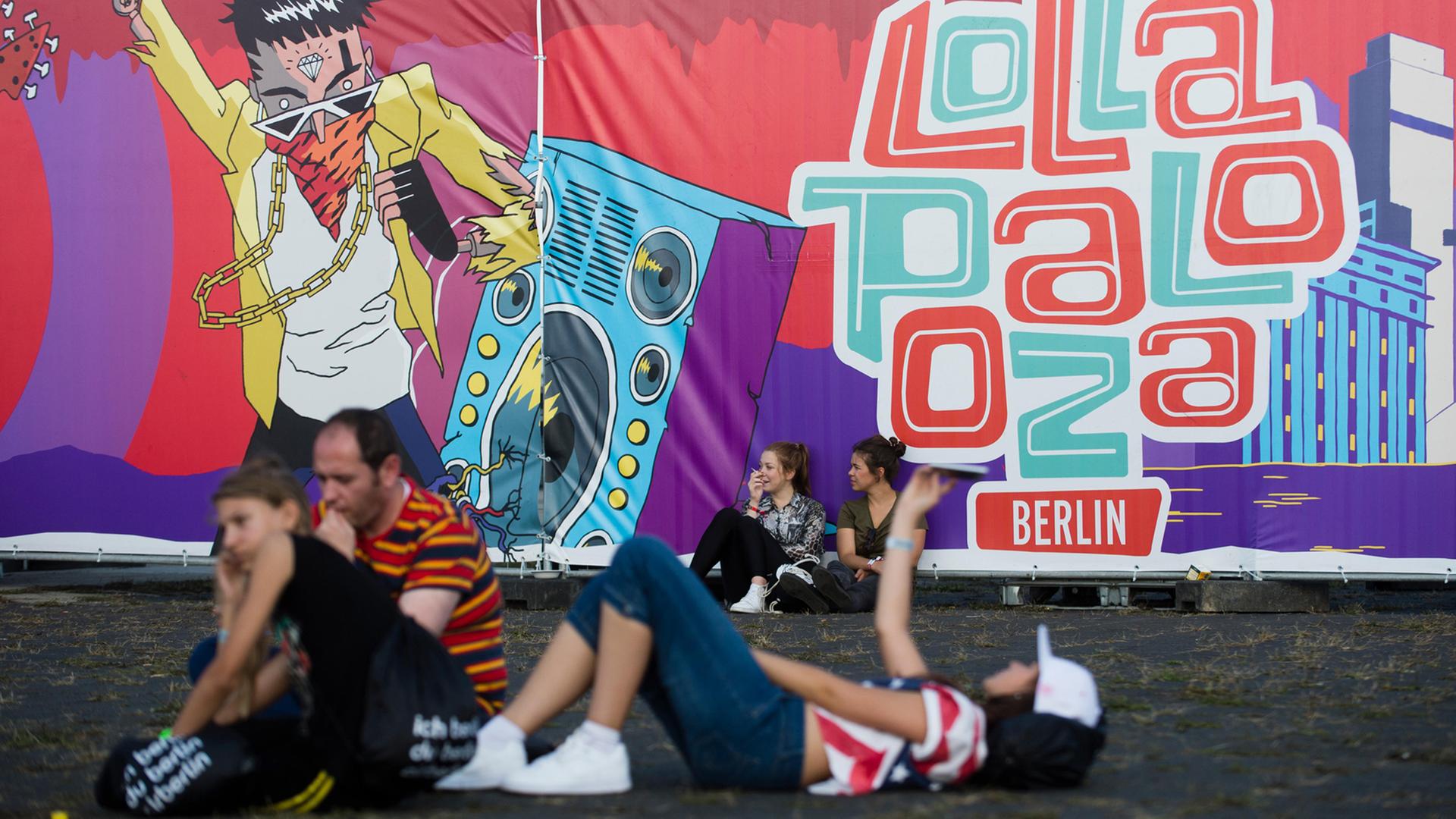Besucher sitzen und liegen am 12.09.2015 vor einer Absperrung mit dem Logo des Lollapalooza Festival auf dem Gelände des ehemaligen Flughafen Tempelhof in Berlin.