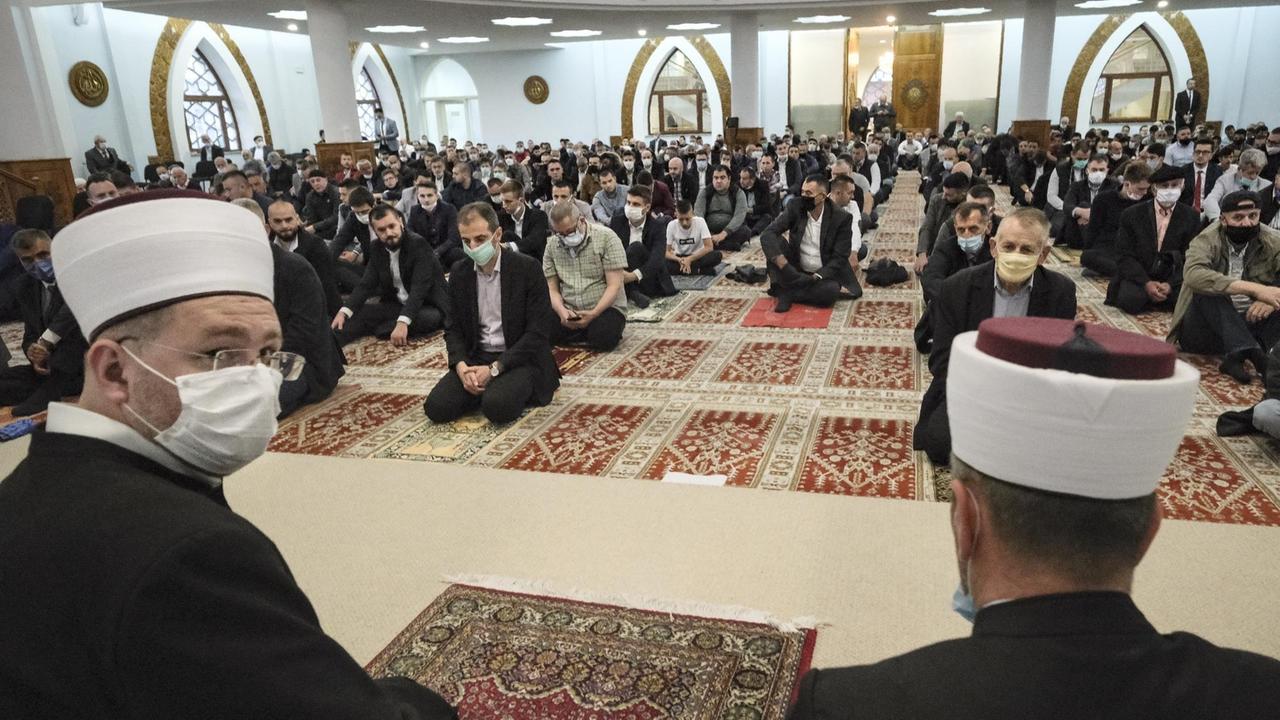 In einer Moschee beten männliche Muslime, sie sitzen mit Abstand zueinander auf dem Boden, viele tragen Mundschutz