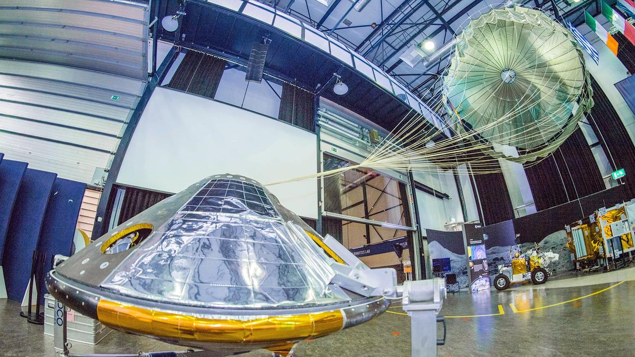 Das silbrige Modell inklusive Fallschirm steht in einer großen Halle.