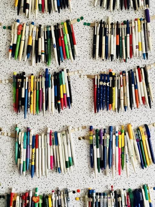 Bunte Kugelschreiber sind säuberlich an einer Wand angebracht.