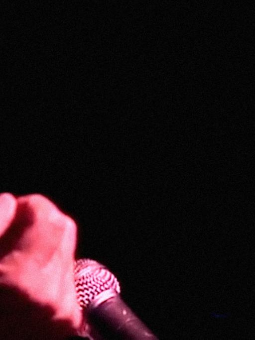 Nahaufnahme von Chavela Vargas während eines Konzertes: Sie singt mit geschlossenen Augen und wird von rotem Licht angestrahlt, der Hintergrund ist dunkel.