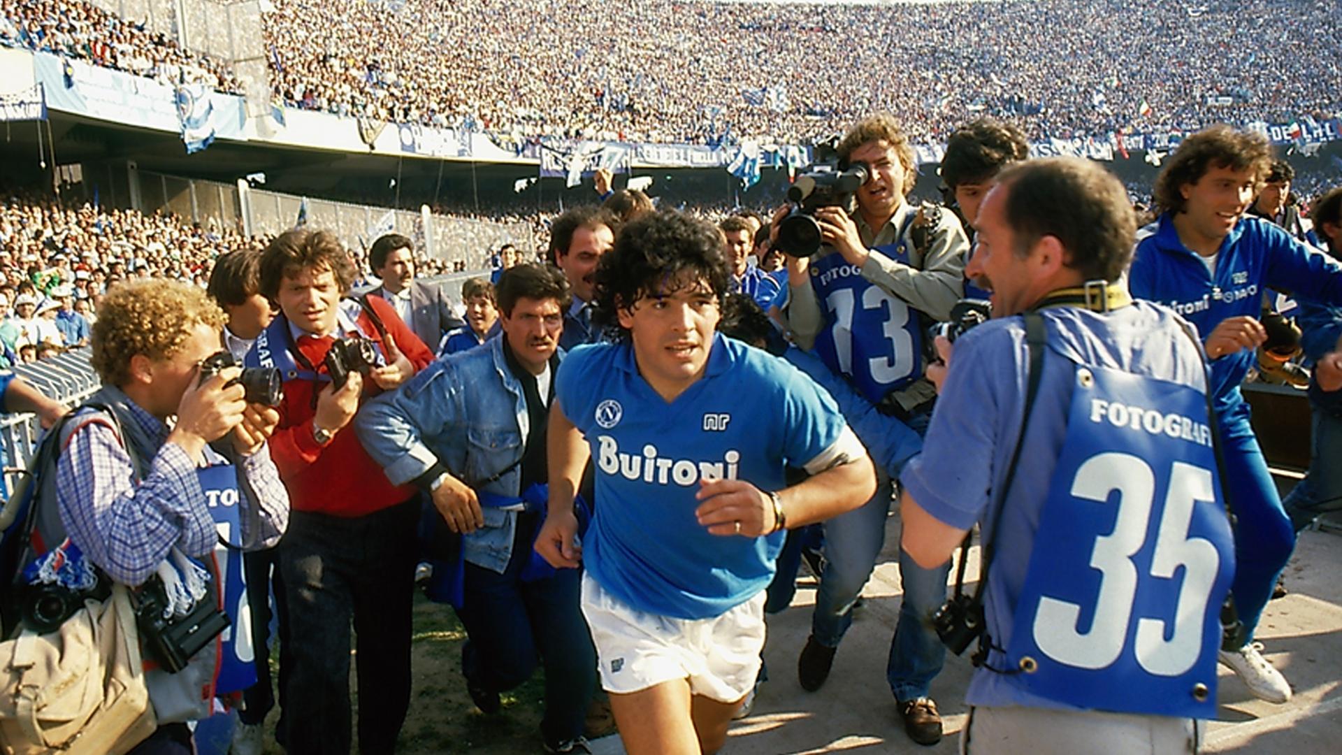 Diego Maradona läuft durch das Stadium, gefolgt von Journalisten.