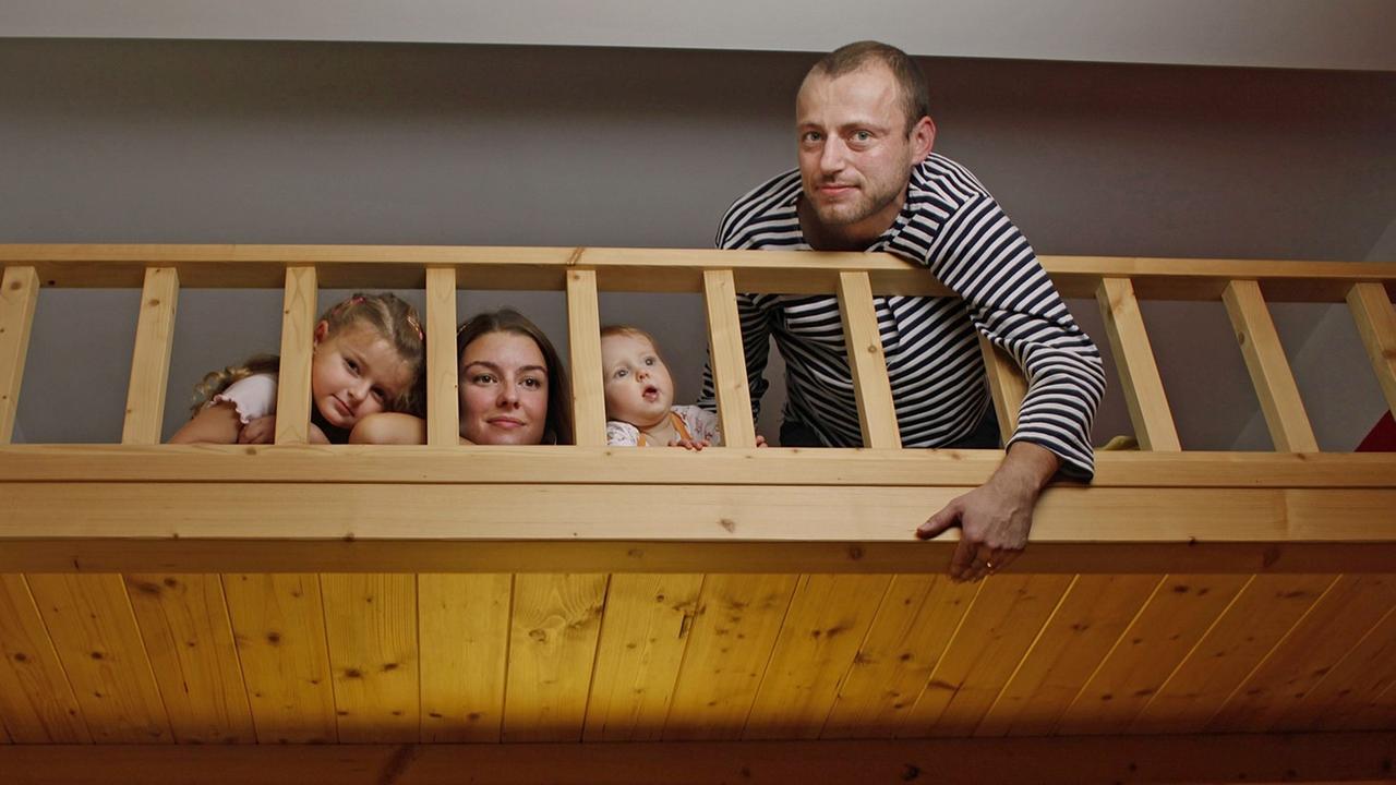 Ein Paar mit zwei Kinder posiert auf einem großen Hochbett für ein Foto.