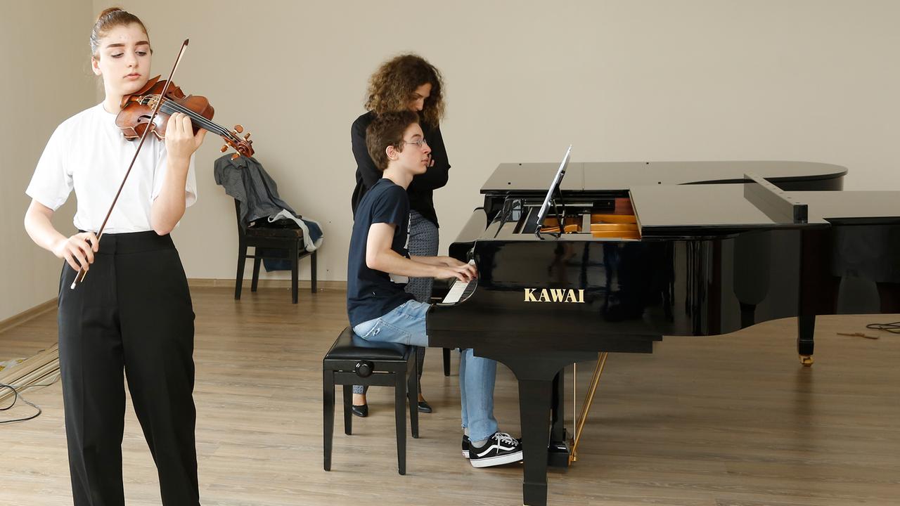 Eine junge Geigerin wird von einem Pianisten begleitet, der an einem Flügel der Firma Kawai sitzt.