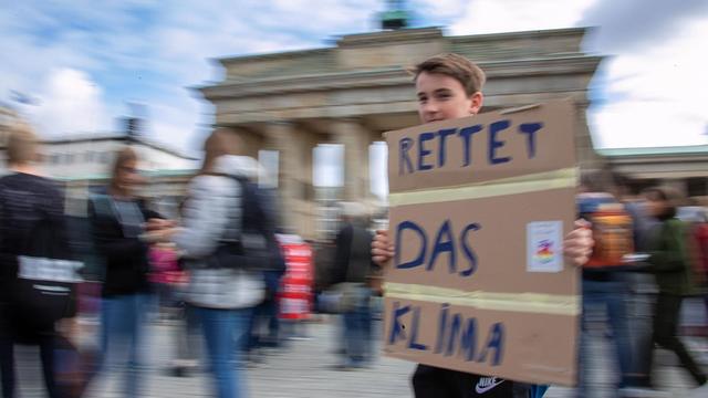 Ein Teilnehmer trägt bei einer Demonstration vor dem Brandenburger Tor ein Plakat mit der Aufschrift "Rettet das Klima".
