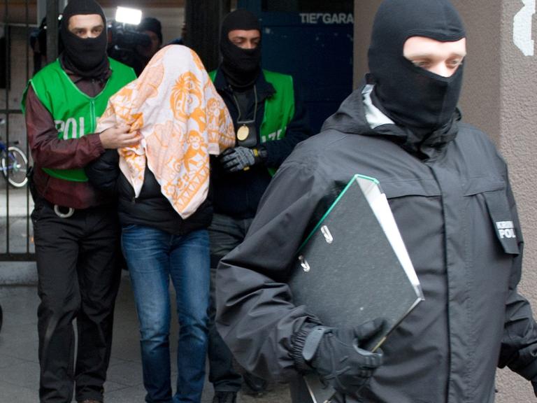 Polizisten führen bei einer Razzia gegen Islamisten am 04.02.2016 in Berlin einen mit einem Tuch verdeckten Verdächtigen ab. Bei Razzien in mehreren Bundesländern hat die Polizei mehrere Islamisten festgenommen, die ein Attentat in Deutschland oder im europäischen Ausland geplant haben sollen
