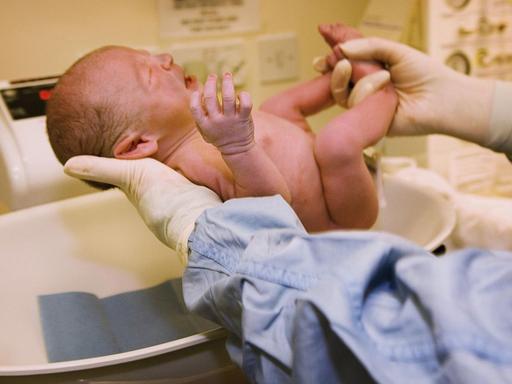 Ein neugeborenes schreiendes Baby wird nach der Geburt von einer Hebamme gewogen.