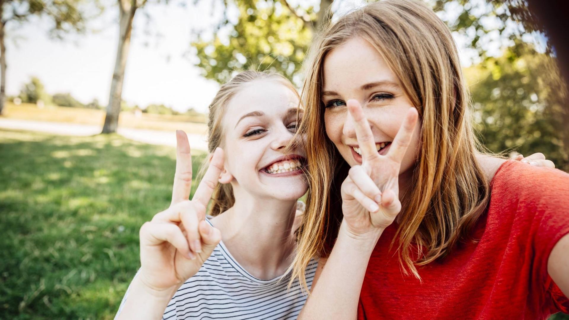Ein Selfie von zwei Teenagerinnen, die grinsend das Victory-Zeichen machen