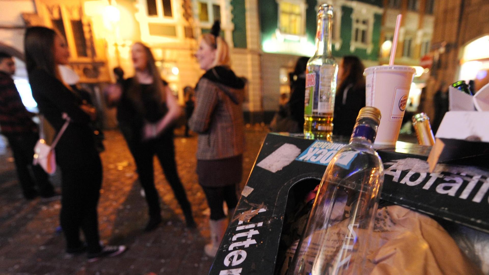 Eine Flasche liegt am Dienstag (21.02.2012) in der Freiburger Fußgängerzone in einem Abfalleimer. Im Hintergrund stehen verkleidete Narren.