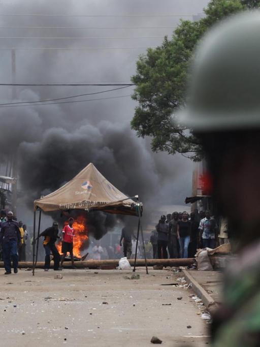 Ein Polizist blickt auf brennende Barikaden und Demonstranten in Kibera, Nairobi