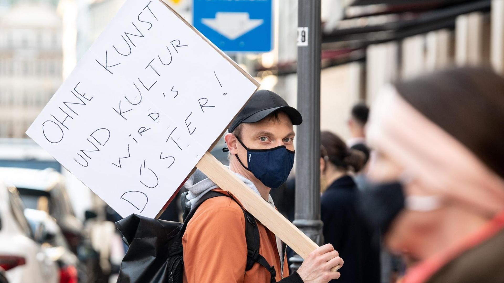 Ein Schauspieler vom Residenztheater steht mit einem Schild mit der Aufschrift „Ohne Kunst und Kultur wirds düster!“ in einer Menschenkette.