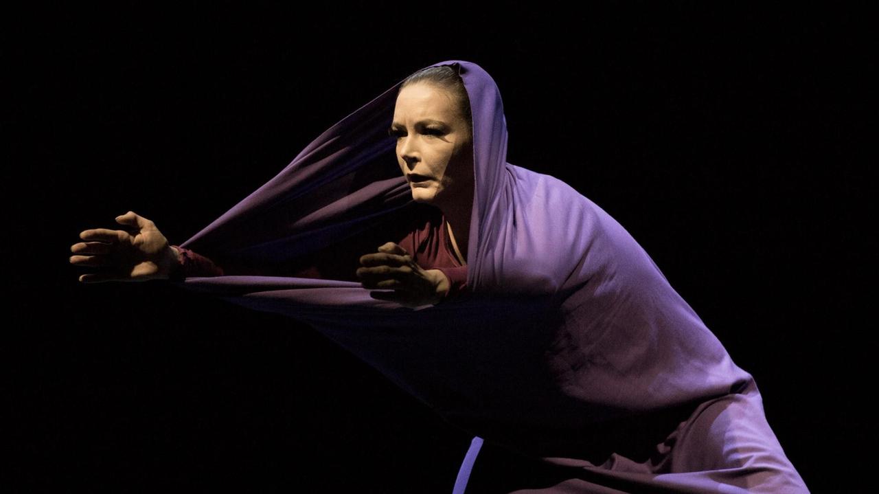 Eine Frau tanzt in einem lilafrabenen Schlauchkleid, das auch ihren Kopf und ihre Arme bedeckt.