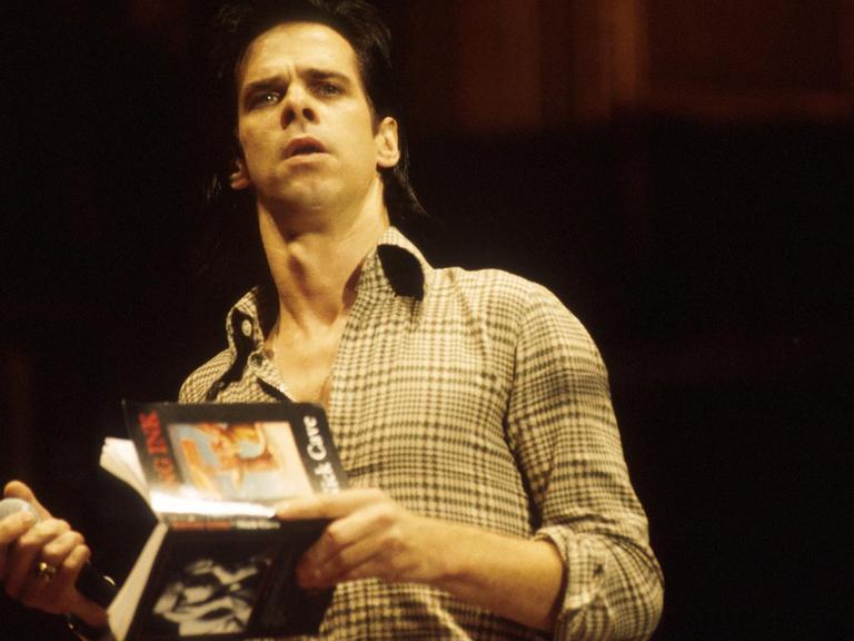Porträt von Nick Cave, der ein Buch in der Hand hält.