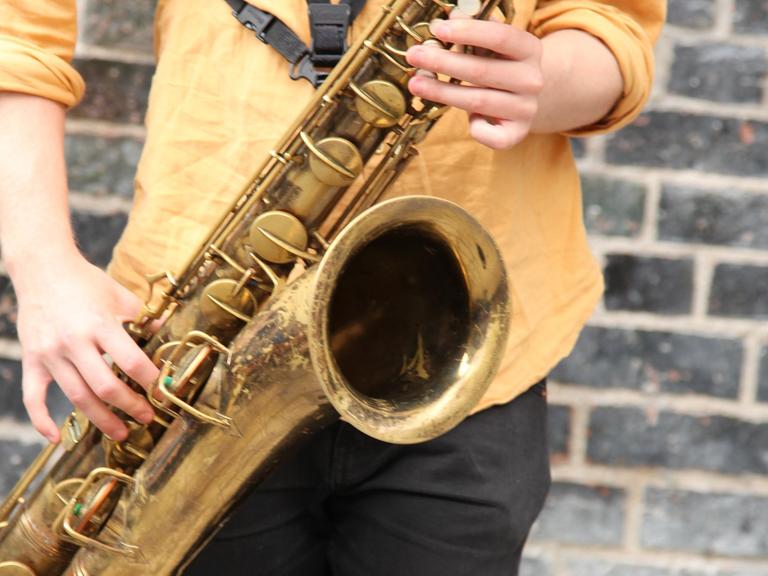 Ein junger Mann spielt in einer Fußgängerzone auf einem Saxofon.