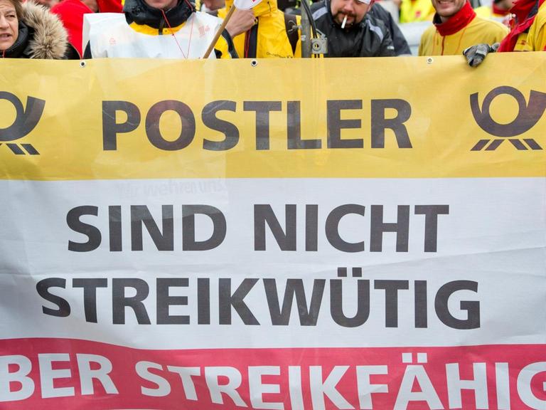 Mitarbeiter der Deutschen Post halten während eines Warnstreiks ein Transparent in die Höhe. darauf steht: ""Postler sind nicht streikwütig aber streikfähig".