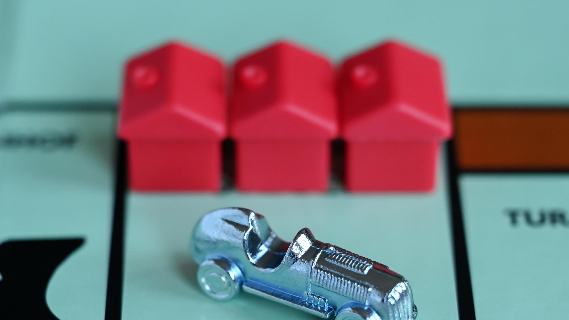 Ein Monopoly-Auto und drei rote Häuschen auf einem Spielfeld