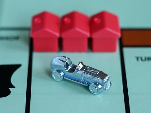 Ein Monopoly-Auto und drei rote Häuschen auf einem Spielfeld