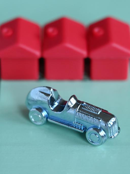 Ein Monopoly-Auto und drei rote Häuschen auf einem Spielfeld